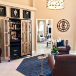 Room has a libation lock, navy blue rug, two brown leather club chairs, large industrial clock on the wall, and framed brass cork screws on the wall for this hip chill lounge.